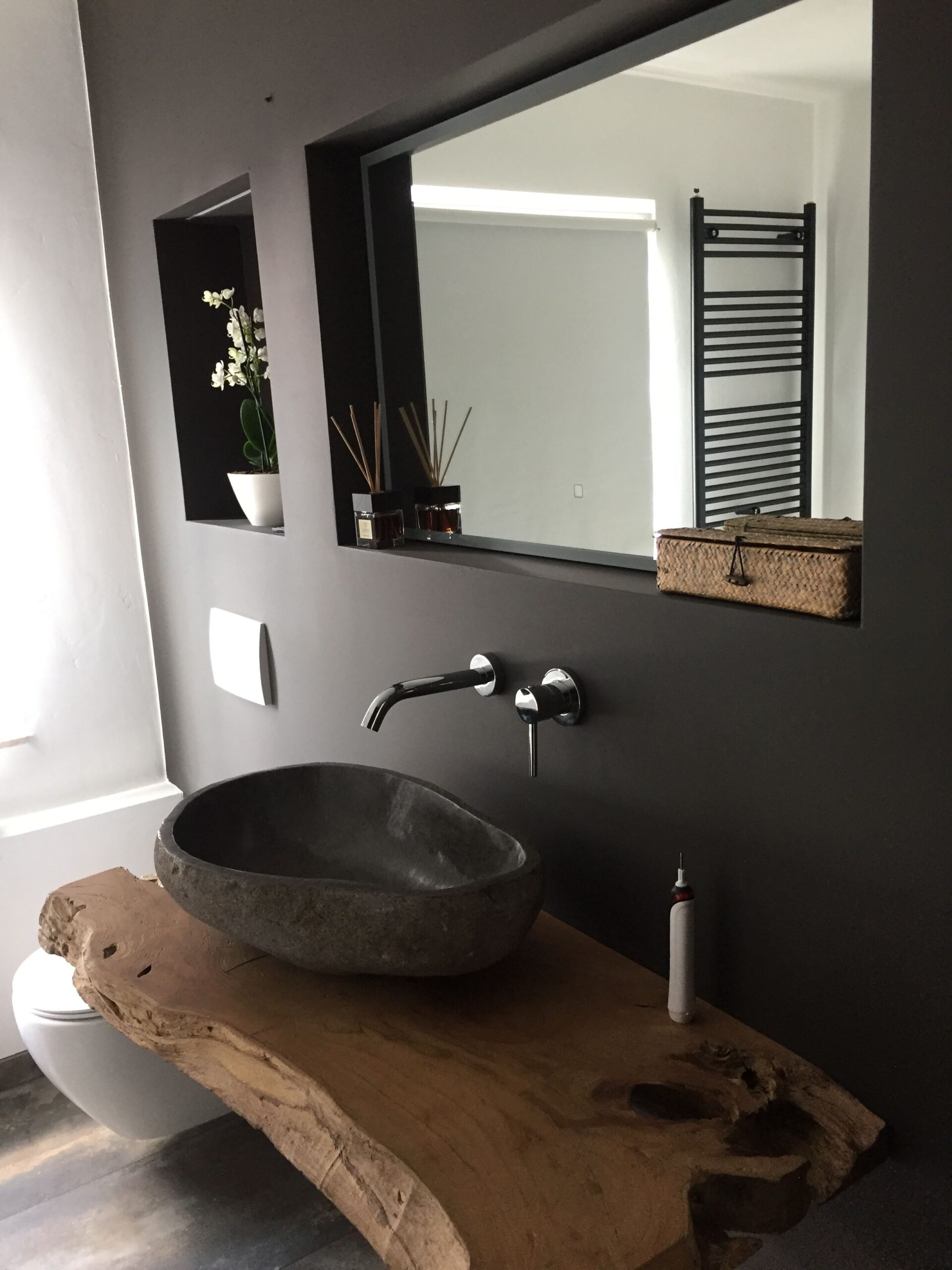elegant and rustic upscale bathroom with thick live edge plank counter, carved stone sink, black wall colour and light and bright shower niche