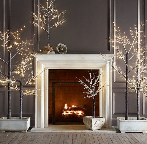 Elegant Christmas decor with fireplace, charcoal wall panelling, and lighted branches in concrete pots