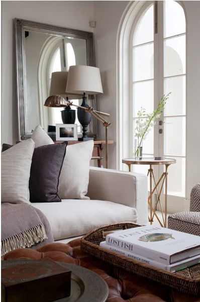 cozy living room with arched French door, leather tufted ottoman, square armed white sofa, leaning mirror, and brass side table