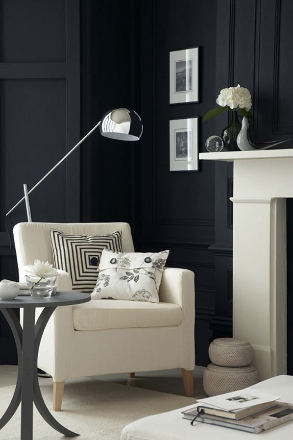 elegant and dramatic sitting area with cream armchair, black and cream toss cushions, cream mantel, and black walls