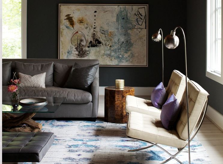 wide view of funky casual living room with muted area rug , tufted sling chairs, grey sofa, purple toss cushions, and large abstract artwork