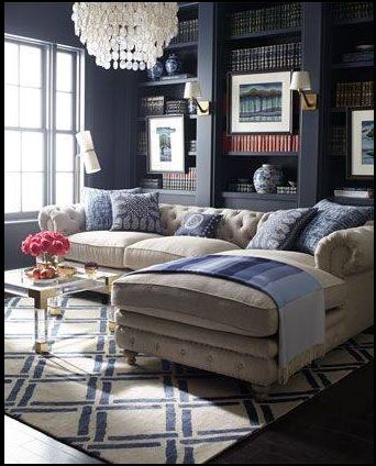 casually elegant living room with dark wall colour, tufted cream sectional, blue toss cushions, geometric area carpet, built-in cabinetry, and shell chandelier