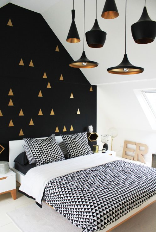 dramatic and interesting bedroom with black and gold feature wall, geometric motif bedding, and many black and gold pendant lights