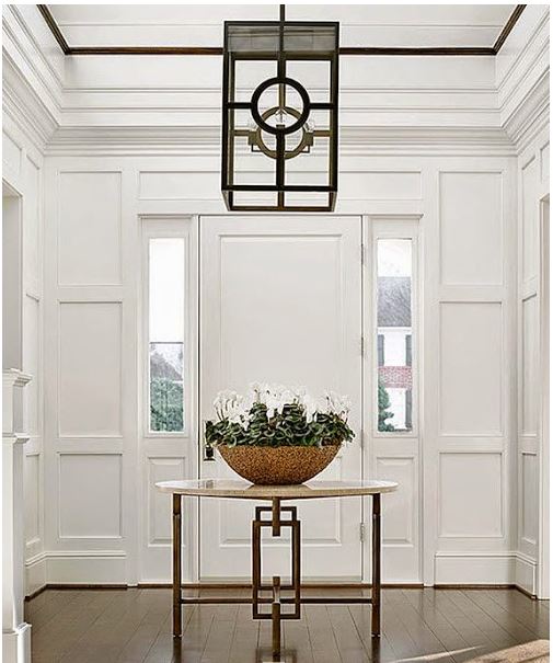 dramatic white foyer with trim moldings, square lantern light fixture, and centre table with bowl of cyclamen