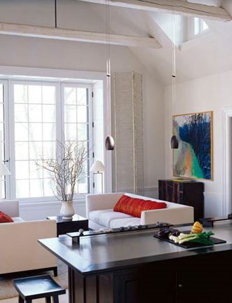 open and airy white living room with paired contemporary sofas with red bolster accent cushions, beamed ceiling, and large abstract artwork in blue