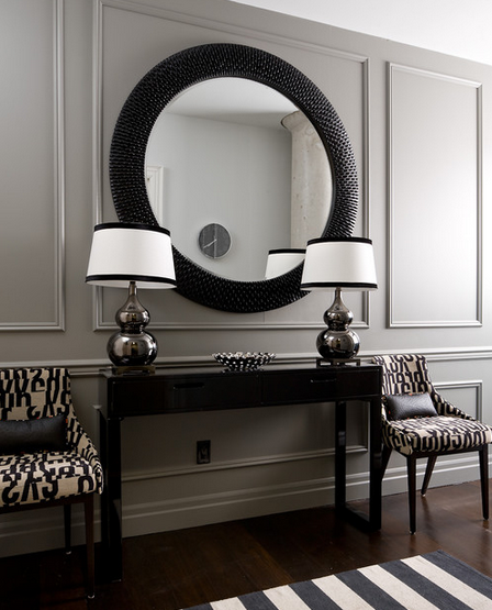 dramatic foyer vignette with black console table and round mirror with paired chairs in black and cream print