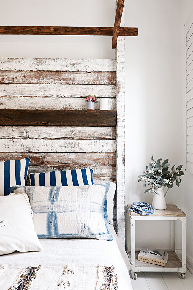 white washed cottage bedroom with tall, rustic wood headboard, blue and white toss cushions, and white walls