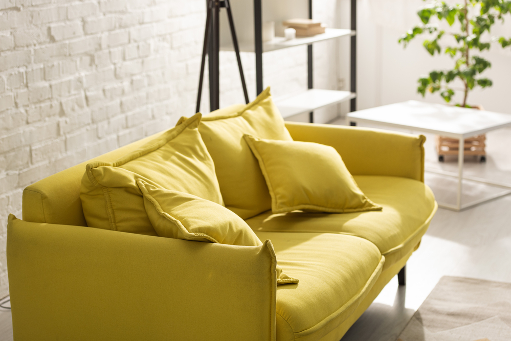 casual and comfortable loft style living room with painted exposed brick wall and yellow sofa