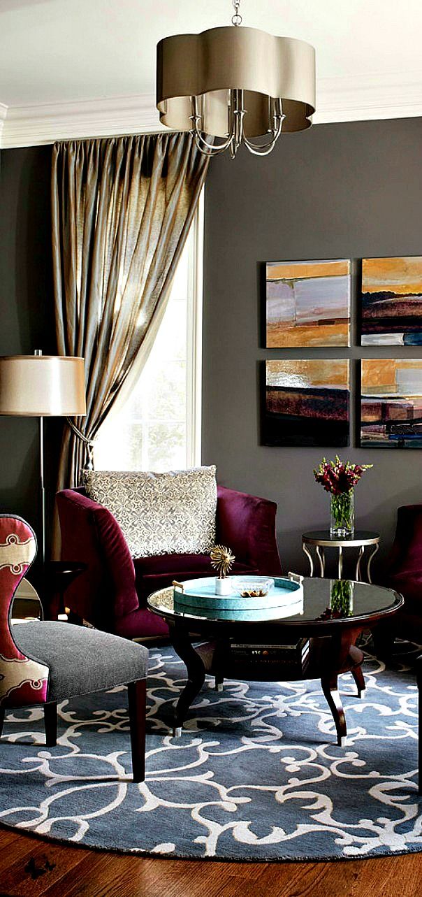 upscale living room in rich colour palette with sideswept custom drapery, graphic area rug, and four abstract artworks in deep gold, burgundy, brown and blue