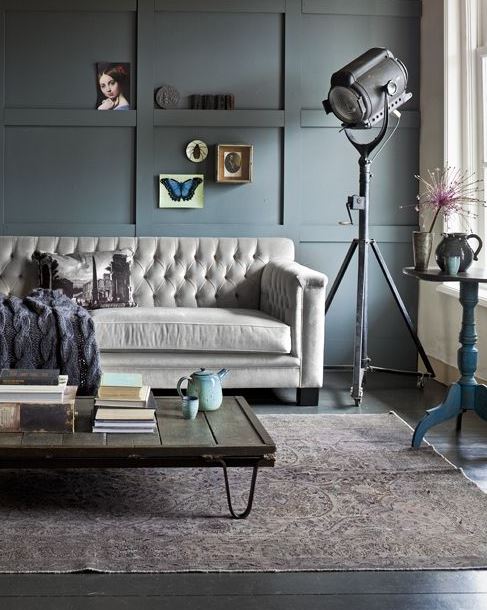 industrial style living room with cream tufted sofa, muted area rug, funky floor lamp, and blue wall panelling
