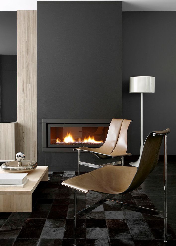 contemporary high style living room with hide area carpet, light wood coffee table, modern fireplace with crushed glass, tan leather chairs, and charcoal mantel tile