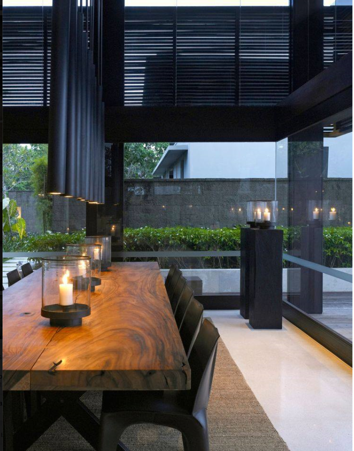 dramatic rusticity in a large dining room with black venetian blinds, tall black pendat lighting , candle vases, and a live edge dining table.