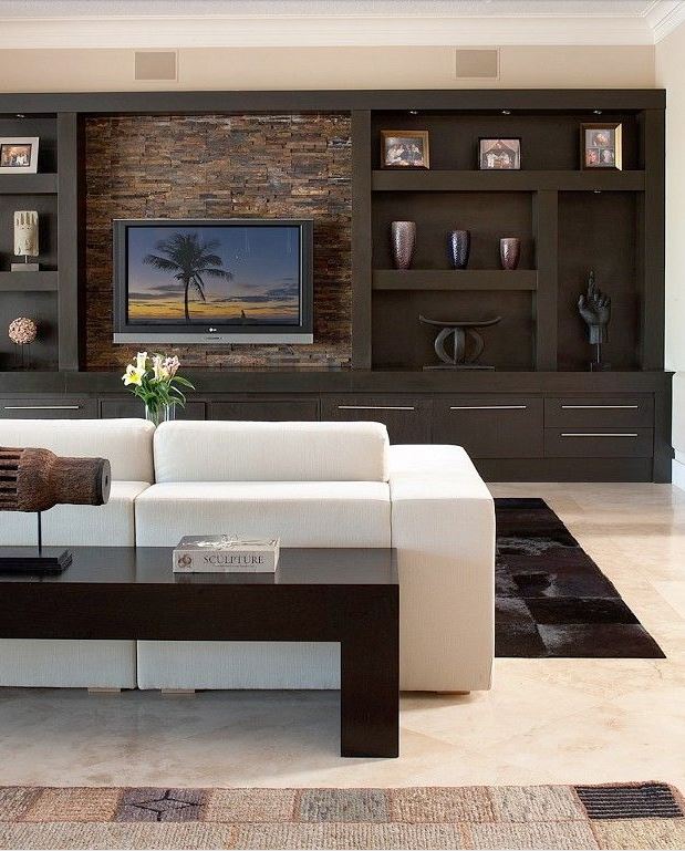 large wall to wall media unit in dark wood with flat screen television, pieced hide area rug, large white sofa, and dark sofa table