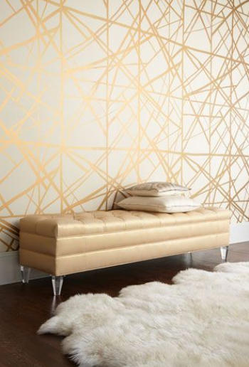 dynamic gold and white geometric wallpaper in a small living room with a tan leather bench