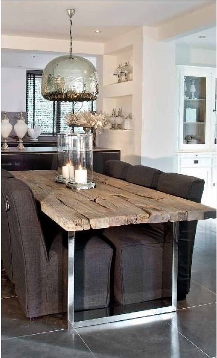 upscale casual dining room with very rustic dining table with chrome legs, Parsons chairs, hurricane vases with candles, and mercury glass pendant light