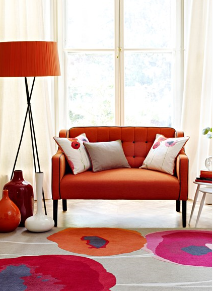 charming small living room with small orange red loveseat sofa and survey style floor lamp with orange shade and funky area rug