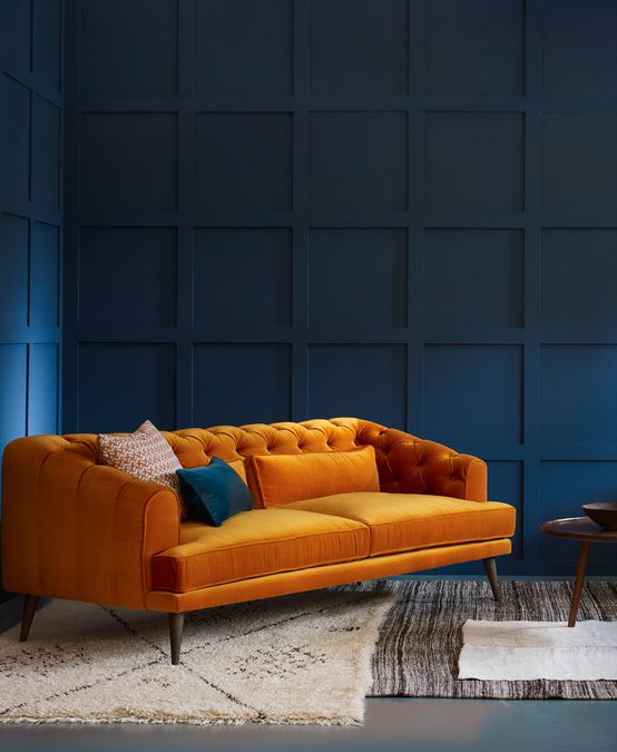 dramatic simple upscal living room with deep blue wall panelling and orange tufted sofa and white area rug