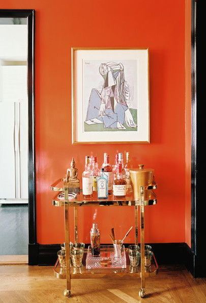 eye-catching room with orange walls, black moldings, and brass cocktail cart with abstract artwork above