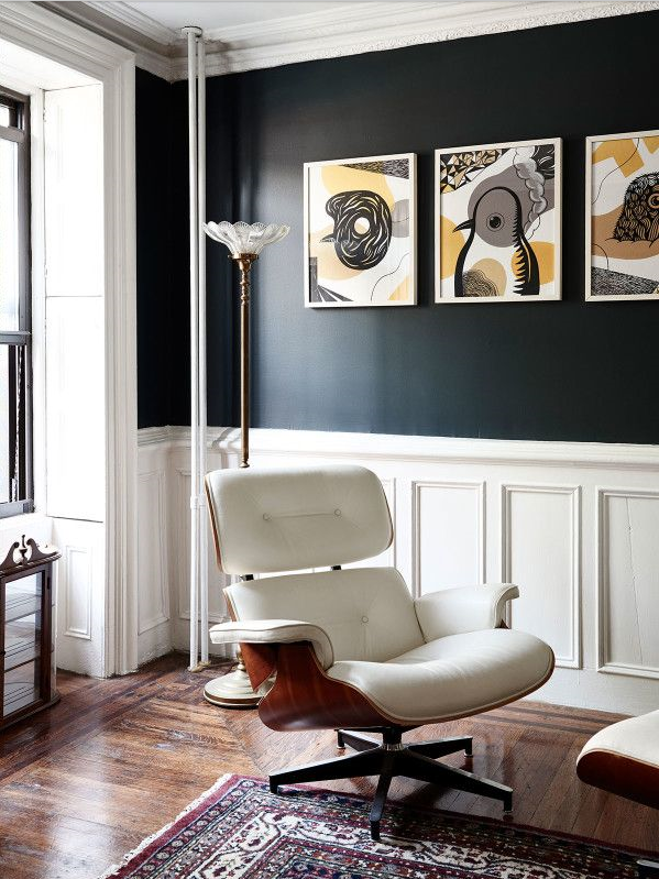 funky condo with white wainscotting and black wall colour, black, gold and white artwork, and white leather Eames chair