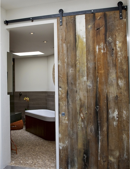 distressed farmhouse style barn door entrance to bathroom with pebble floor