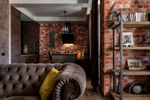 charming and funky casual smaller home with red exposed brick, mushroom grey velvet buton tufted sofa, rustic wood and metal open shelving and hardwood flooring