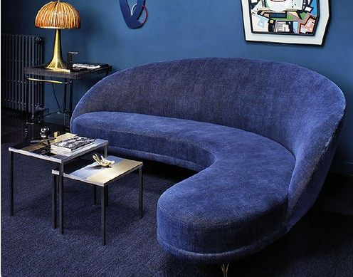 wide view of small living room in deep blue with curved and funky blue loveseat with small abstract art pieces in a small living room